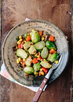 a bowl filled with vegetables sitting on top of a wooden table next to a fork