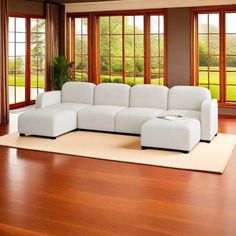 a large white couch sitting on top of a wooden floor in front of two windows