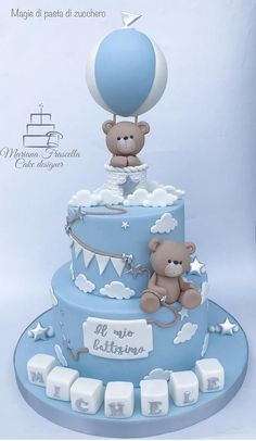 a blue and white cake with a teddy bear on top that has a hot air balloon above it