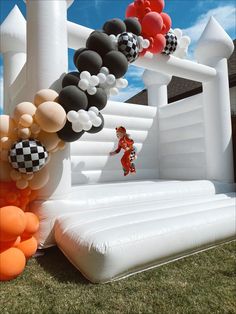 an inflatable bouncer and some balloons on the grass with a person jumping over it