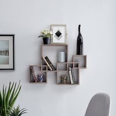 a wall mounted shelf with books, vases and pictures on it next to a chair