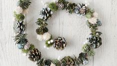 a wreath made out of pine cones and succulents on a white wooden surface