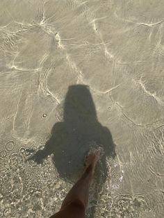 a person standing in shallow water with their shadow on the sand and bottom of them