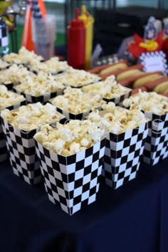 some food is sitting on a table with checkered paper cups and hotdogs