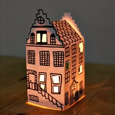 a lit up paper house sitting on top of a wooden table next to a window