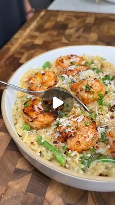 a white bowl filled with pasta and shrimp on top of a wooden table next to a knife