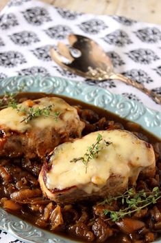 two meats covered in gravy sit on a blue plate next to a spoon