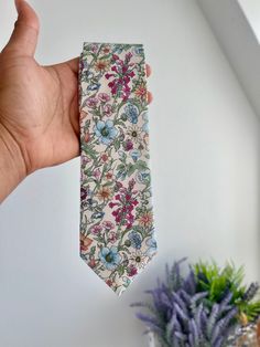 a hand holding a floral tie next to a potted plant on a white wall