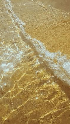 an airplane is flying low over the water at the edge of the beach, with waves coming in from the shore