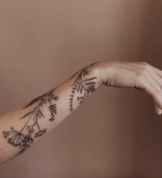 a woman's arm with flowers and leaves tattooed on her left arm, in front of a brown wall