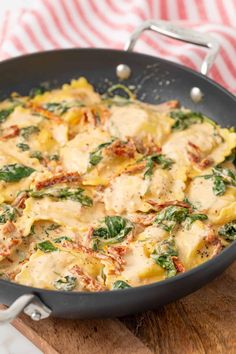 a pan filled with pasta and spinach on top of a wooden cutting board