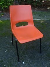 an orange plastic chair sitting on top of a black metal frame in front of some bushes