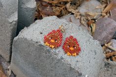 a pair of red and yellow beaded chicken earrings sitting on top of a rock