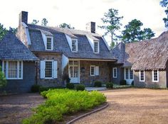 an old brick house with white windows and shingles on the roof, surrounded by greenery