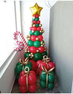 a christmas tree made out of balloons and wrapped in gold, red and green ribbons