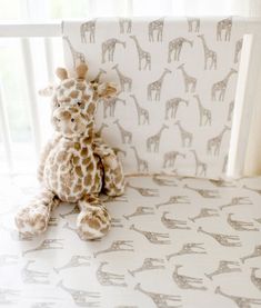 a stuffed giraffe sitting on top of a bed next to a wallpaper