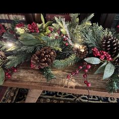 a wooden table topped with pine cones and greenery next to a fire place covered in christmas lights