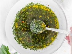 a white bowl filled with green soup on top of a table next to a spoon