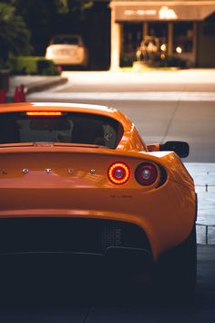 an orange sports car parked on the side of the road at night with its lights on