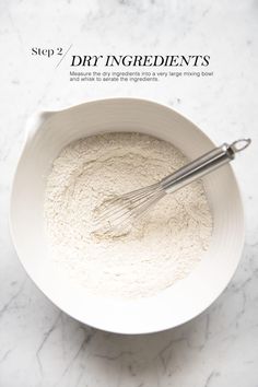 a white bowl filled with dry ingredients next to a whisk on top of a marble counter