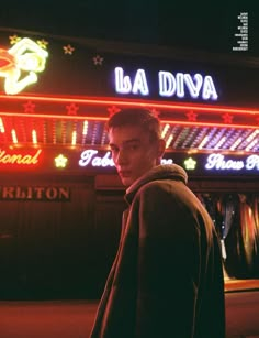 a man standing in front of a neon lit building with the name la diva on it