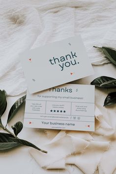 thank you cards sitting on top of a bed next to green leaves and white sheets