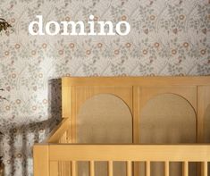 a wooden crib in front of a floral wallpaper with the word domino on it