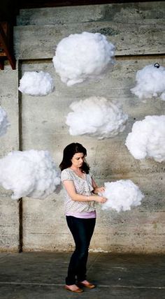 a woman standing in front of a cement wall with white clouds floating above her head