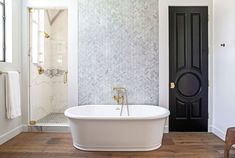 a white bath tub sitting in a bathroom next to a wooden floor and black door