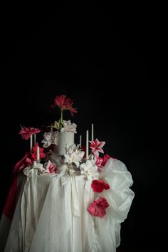 a white cake with pink flowers and candles sitting on top of the table in front of a black background