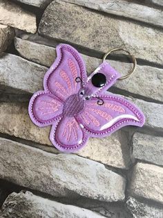 a purple butterfly keychain sitting on top of a stone wall