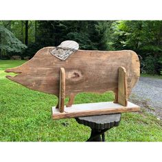 a wooden pig sculpture sitting on top of a bench in the grass next to trees