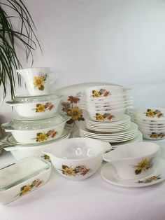 a table topped with lots of white dishes and bowls filled with flowers on them next to a potted plant