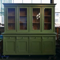 a green china cabinet with glass doors and drawers on wheels in a room filled with other furniture