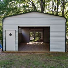 an open garage door on the side of a white building with trees in the background