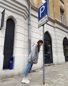 a woman leaning against a parking sign on the side of a street in front of a building