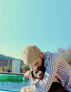 a man sitting on the edge of a swimming pool holding a dog in his lap