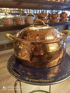 a large copper pot sitting on top of a metal stand in front of some shelves