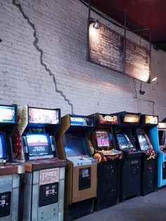 several arcade machines lined up next to each other in front of a white brick wall