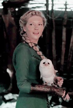 a woman holding an owl on her arm while wearing a green shirt and black gloves