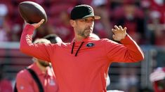 a man holding a football in his right hand and wearing a red shirt with black on it