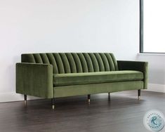 a green velvet couch sitting on top of a hard wood floor next to a window