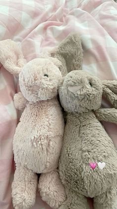 two stuffed animals laying next to each other on a pink and white checkered blanket