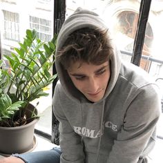 a young man sitting in front of a potted plant looking at his cell phone