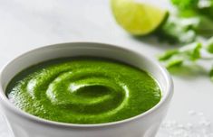 a white bowl filled with green liquid next to limes