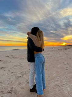 two people embracing each other on the beach at sunset or sunrise with clouds in the sky