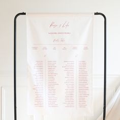 a wedding seating chart hanging on a metal stand in front of a white wall and door