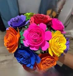 a bouquet of multicolored paper flowers in someone's hand on a table