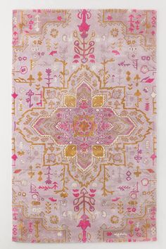 a pink and gold rug with an intricate design on the bottom, in front of a white wall