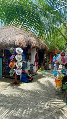 an outdoor market with lots of hats and umbrellas on the sidewalk near palm trees